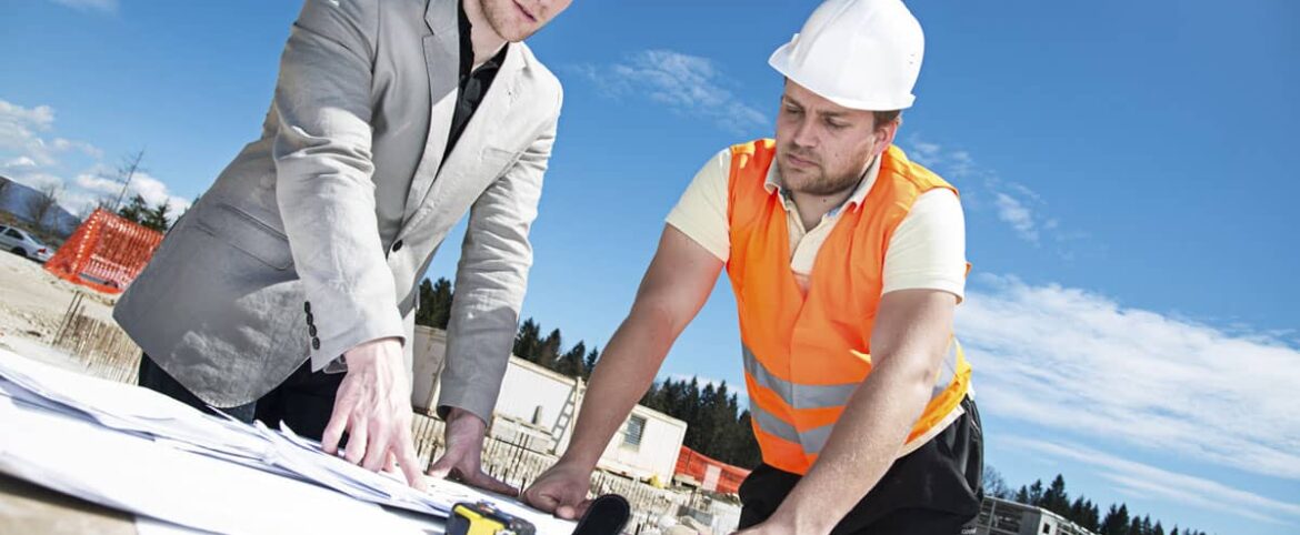 Two men in hard hats and vests working on a building.