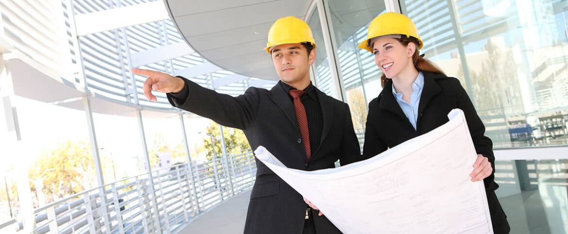 Two people in hard hats pointing at a building