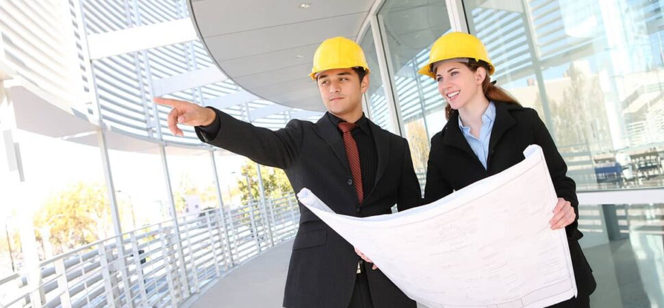 Two people in hard hats pointing at a building